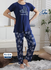 A woman modeling a two-piece pajama set in a bright bedroom setting. The set includes a navy blue short-sleeve top with a crescent moon and stars graphic and the text 'Time to sleep,' paired with navy blue pants featuring a white floral pattern.